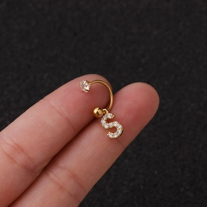 Détail d'une boucle d'oreille C dorée avec pendentif lettre S en zircon et boule
