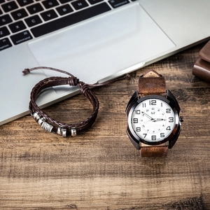 Men's quartz watch with leather strap and braided bracelet on a wooden desk setup