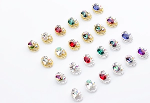 Close-up of oval rhinestone nail charms with twisted metal edges and pearl accents