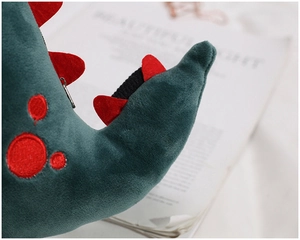 Macro shot of green plush dinosaur bag featuring red spots and metal zipper detail