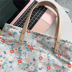 Close-up of floral canvas tote bag featuring leather handles and golden metal rivets