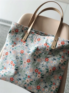 Floral canvas tote bag with gray-blue base and premium brown leather handles detail