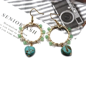 Detail view of bohemian gold hoop earrings with green beads and heart turquoise pendant