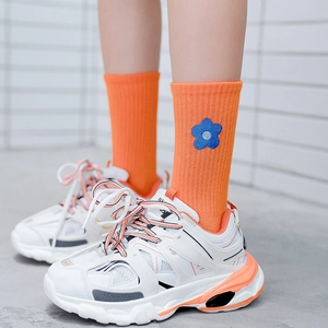 Orange mid-calf socks with blue flower embroidery shown with sneakers on a white wall