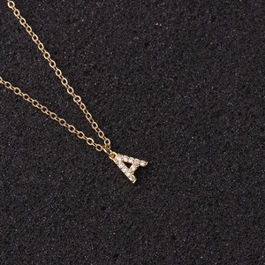 Macro shot of gold letter A pendant with clear zircons on black textured background