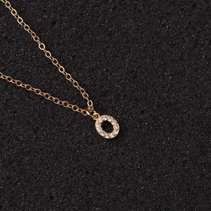 Detail shot of golden necklace with a zircon-inlaid letter O pendant on black texture