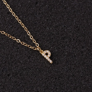 Detailed close-up of gold initial P necklace with sparkling zircon pavé on black sponge