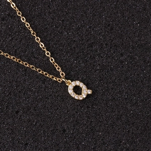 Macro shot of gold letter Q pendant with zircon stones on a black textured background