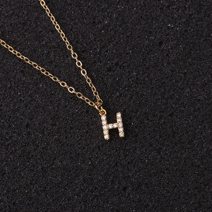 Close-up of golden letter H pendant with zircon stones on a black textured surface