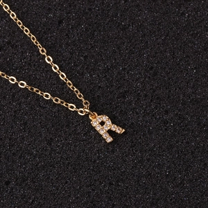 Close-up of golden necklace with letter R pendant inlaid with clear zircon stones