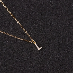 Detailed view of golden letter L pendant necklace with cubic zirconia on black texture