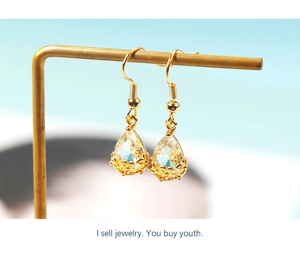 Macro detail of teardrop crystal earrings featuring intricate gold hollow floral base