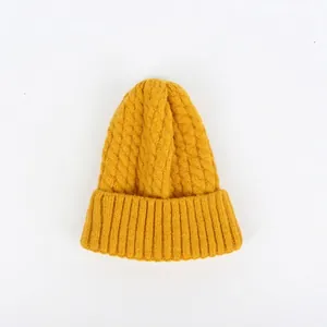 Detailaufnahme der dicken Zopfmuster-Textur auf einer warmen ingwergelben Winter-Strickmütze