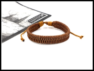 Close-up of brown braided leather bracelet with adjustable cord on white surface