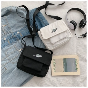Detail of planet embroidery on canvas crossbody bag with adjustable strap and casual props