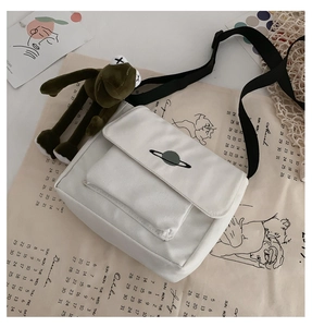 Detail of white canvas crossbody bag featuring green planet embroidery and black strap