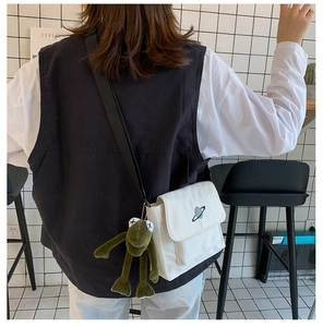 White canvas messenger bag with planet embroidery and green frog plush pendant on model