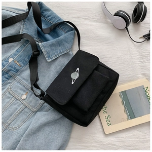 Detail of black canvas crossbody bag with planet embroidery next to a denim jacket