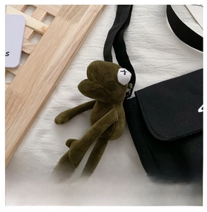 Close-up of a green plush frog keychain with X-shaped eyes on a black canvas bag