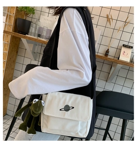 Detail of white canvas crossbody bag featuring planet embroidery and plush frog charm