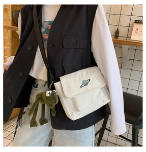Detail of white canvas crossbody bag with planet embroidery and green frog charm on a model