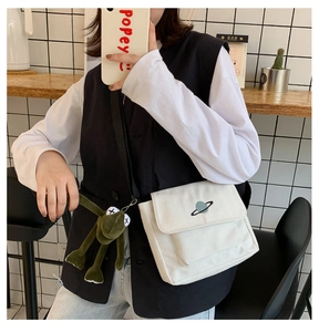 Detail view of a white canvas crossbody bag with planet embroidery on a lifestyle model