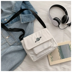 Detailed flat lay of white canvas satchel with Saturn embroidery and black strap