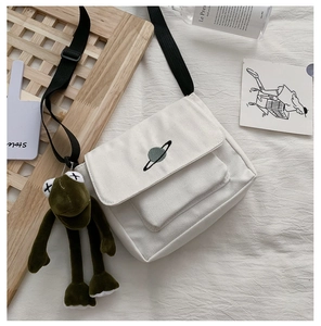 Detail of white canvas crossbody bag with planet embroidery and green frog charm