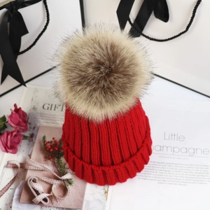 Flache Liegeansicht einer roten Strickmütze mit flauschigem Kunstfellbommel als Geschenk