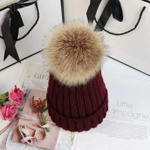 Detail der weinroten Strickmütze mit flauschigem khakifarbenem Pelzbommel als Geschenk