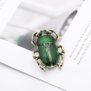 Detail view of a vintage gold insect brooch with emerald green enamel and black bead eyes
