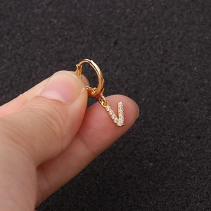 Gros plan d'une boucle d'oreille dorée en forme de V sertie de zircons entre les doigts