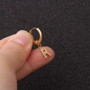 Gros plan d'une boucle d'oreille anneau dorée avec un pendentif lettre R en zircone