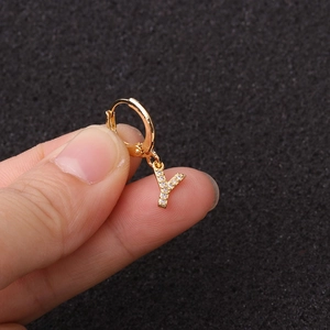 Gros plan sur une boucle d'oreille dorée lettre Y avec zircons tenue par les doigts