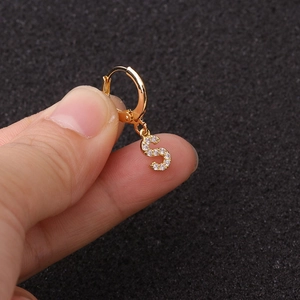 Gros plan sur boucle d'oreille lettre S dorée avec zircons sur fond sombre texturé