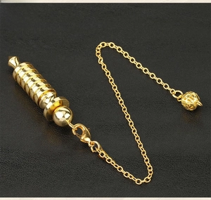 Macro shot of a golden spiral metal pendulum with chain on black textured leather