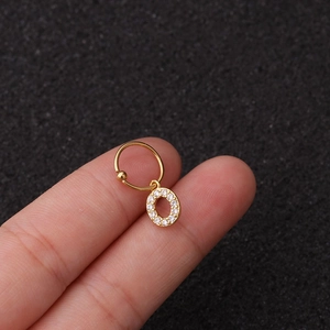 Détail macro d'une boucle d'oreille pendante dorée lettre O avec incrustation de zircon