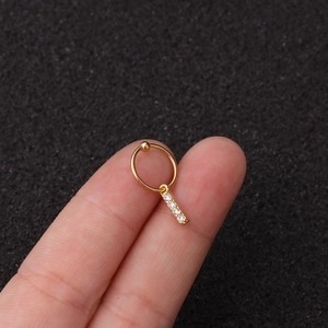 Vue macro de la boucle d'oreille cartilage en acier doré avec pendentif barre zircon