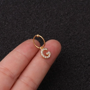 Vue macro du piercing lettre G dorée avec zircons brillants et finition polie soignée