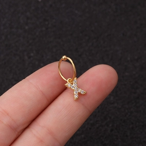 Vue macro d'une boucle d'oreille dorée avec pendentif lettre X et zircons sur un bout de doigt