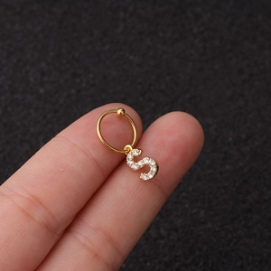 Vue macro d'un pendentif lettre S doré serti de zircons tenu à la main