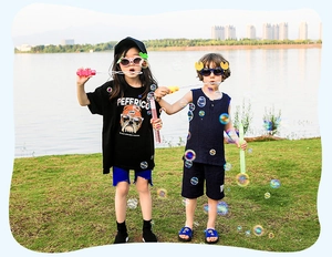 Kids outdoors playing with small colorful bubble wands near lake in summer outfits