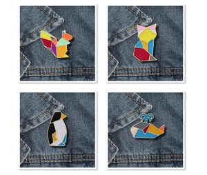 Vue détaillée de quatre pins émaillés en origami géométrique coloré sur du denim