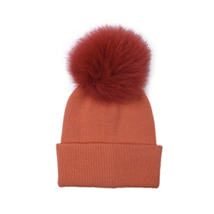 Soft orange knit beanie hat featuring a large burgundy fluffy fur pompom on top.