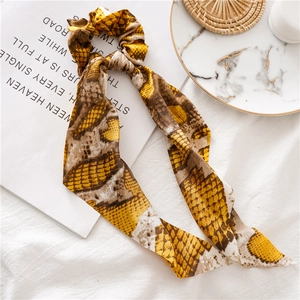 Detail view of yellow python print scrunchie with long ribbons on marble background
