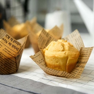 Details von fettbeständigen Muffinformen mit Vintage-Zeitungsdruck in einer Backszene