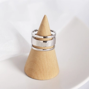 Three layered silver rings with different widths on a minimalist wooden cone stand