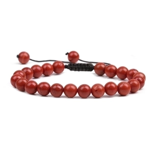 Detail of red stone beaded bracelet with adjustable black braided cord on white background