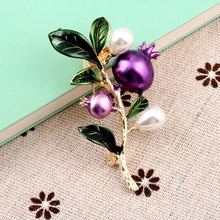 Detailed close-up of golden brooch with green enamel leaves and purple pearl pomegranates