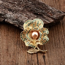 Golden flower brooch with green rhinestones and a central pearl on a wooden texture
